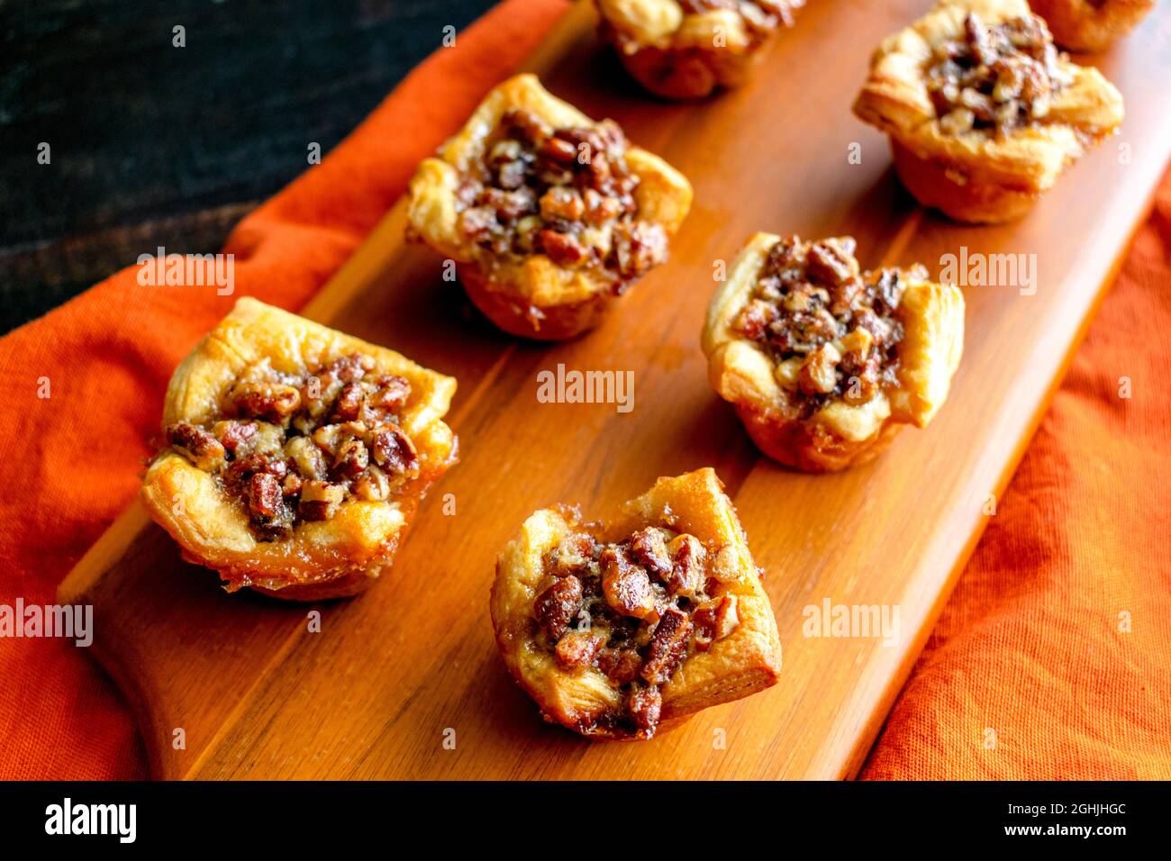 Pecan Pie Tartelettes serviert auf einem Holzschneidebrett: Einzelne Pecan Pie Tarteletten werden auf einem Holzschneidebrett angezeigt Stockfoto