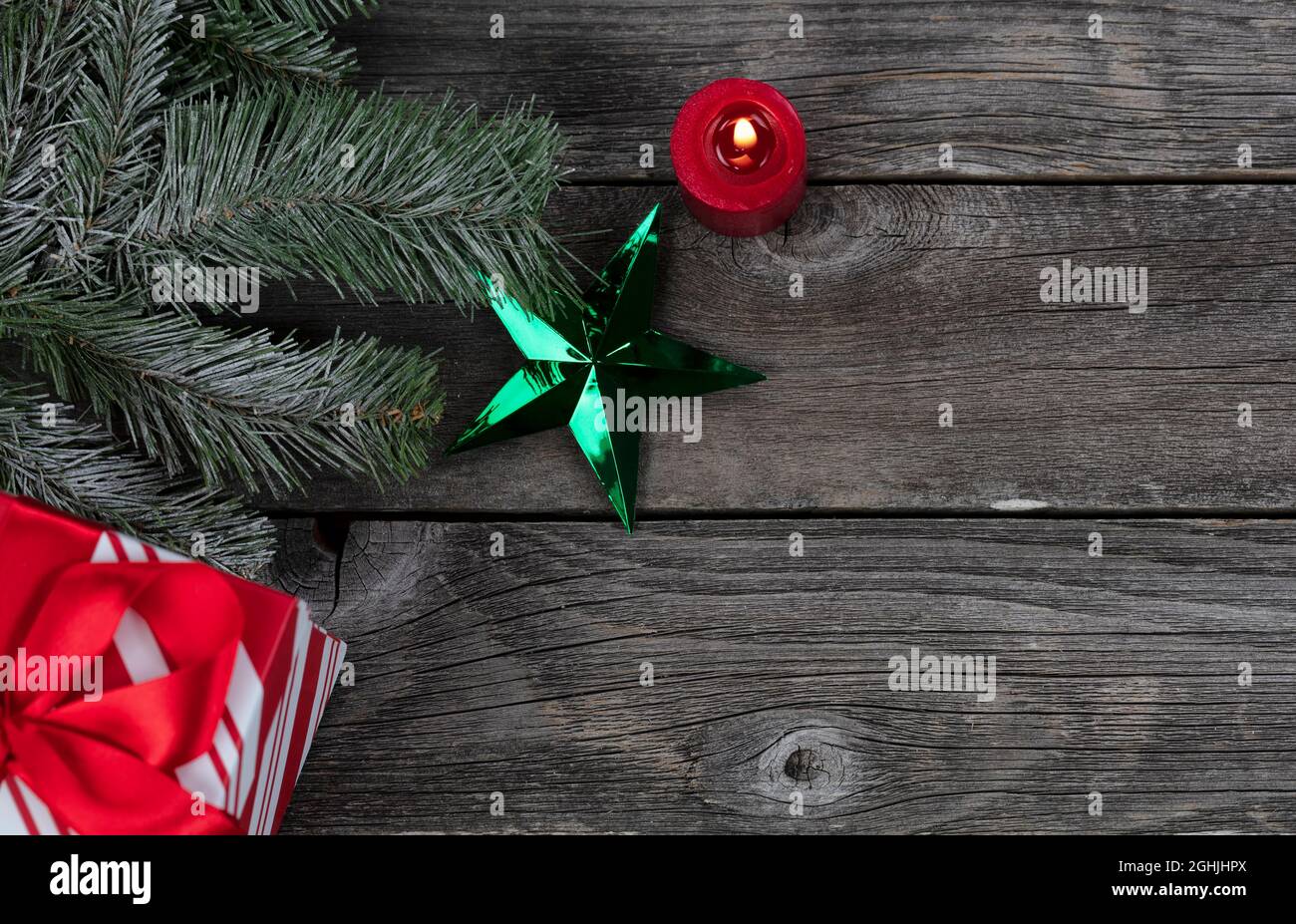 Ein grüner Stern Ornament und leuchtende Kerze, Geschenkbox plus Schneetanne Zweig Dekorationen auf rustikalen Holzplanken für ein fröhliches Weihnachten oder glückliches Neues Ye Stockfoto