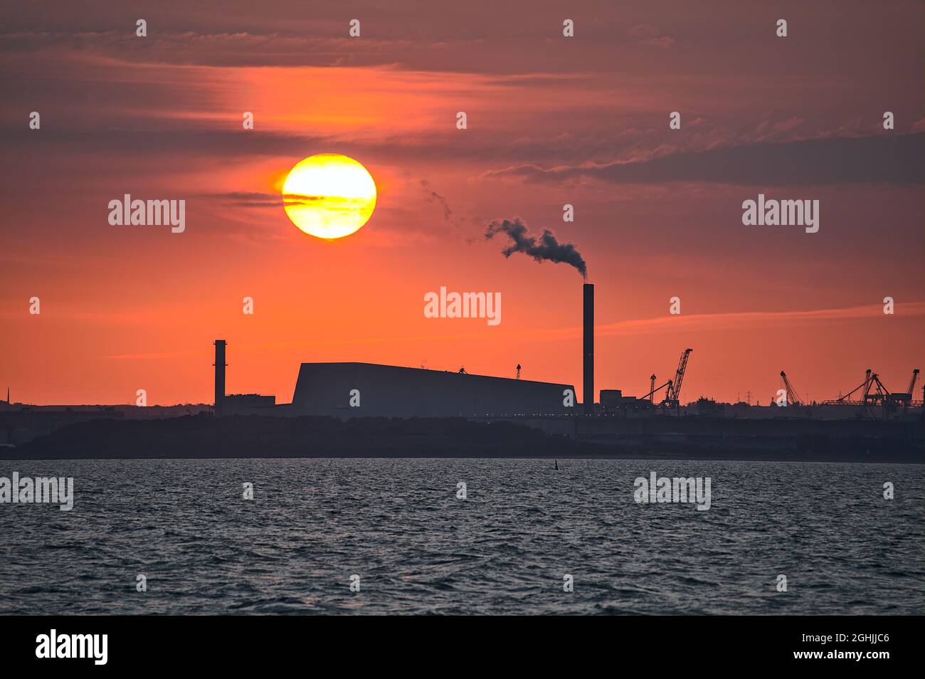 Teleansicht des epischen orangen Sonnenuntergangs über dem Hafen von Dublin und der Sonne, die mit dem Werk Covanta (Dublin Waste to Energy) in Einklang steht, vom westlichen Pier von Dun Laoghaire aus gesehen Stockfoto