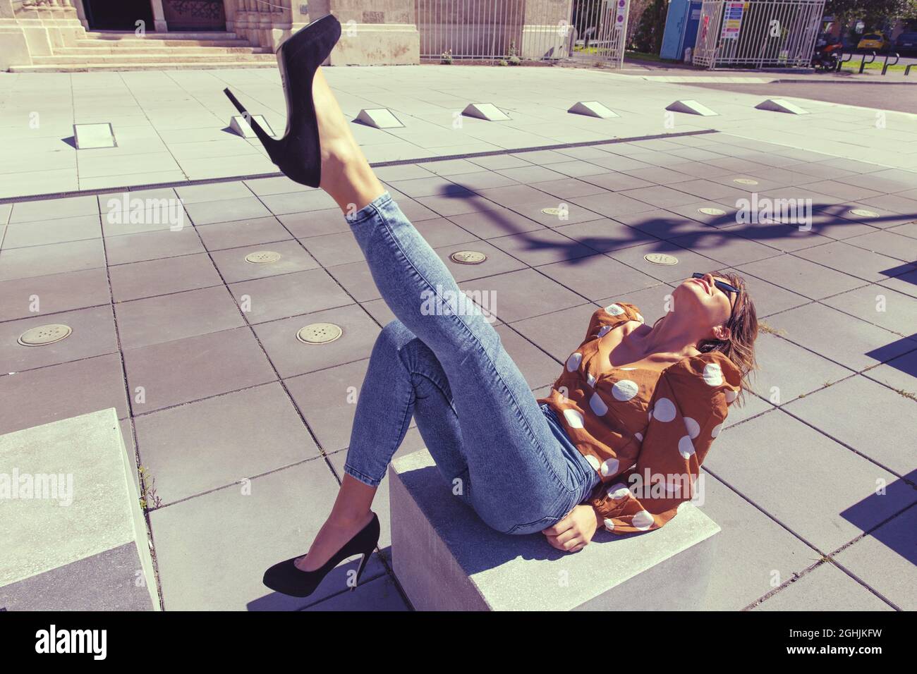 Stilvolle junge Reisende Frau sitzt auf Stein an berühmten Ort in der Stadt, Bein nach oben Stockfoto