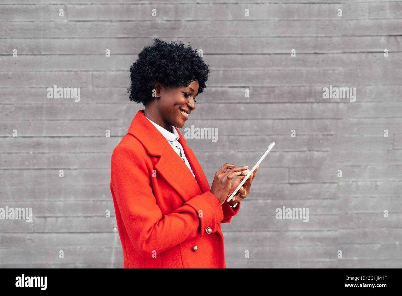 Stilvolle afroamerikanische Frau lächelt, während sie ein digitales Tablet draußen auf der Straße benutzt. Stockfoto