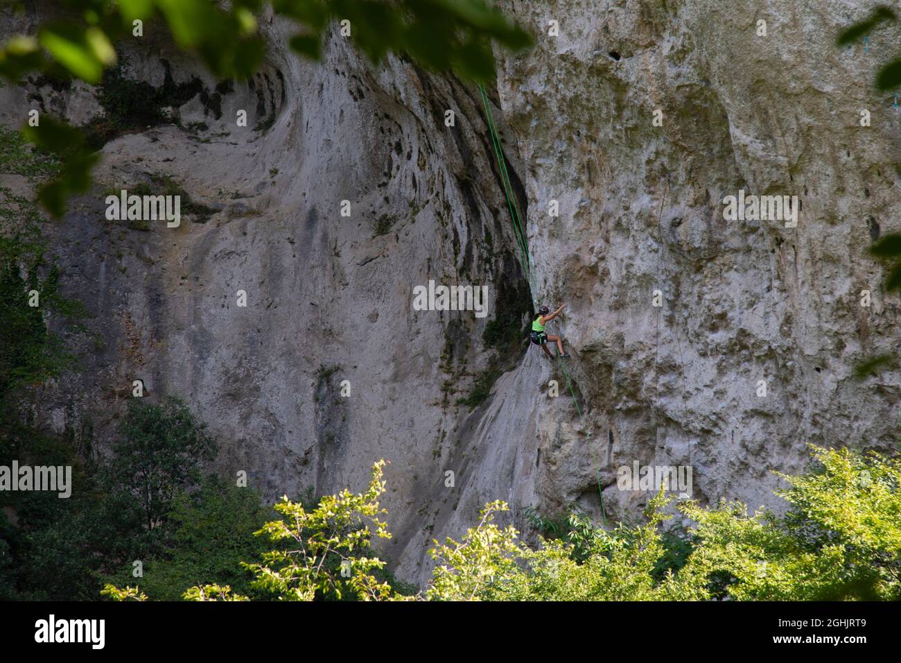 Blick aus der Ferne auf eine steile Klippe in den italienischen Alpen, kleine Figuren von Kletterern, die sie besteigen Stockfoto