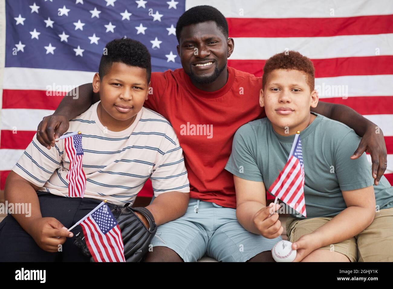 Porträt eines afroamerikanischen Mannes, der Söhne im Teenageralter gegen die amerikanische Nationalflagge umarmt Stockfoto