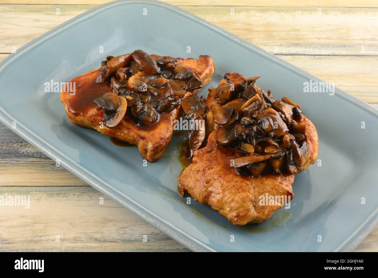 Zwei knochenlose Schweinekoteletts mit brauner Pilzsauce auf blauem Servierteller Stockfoto