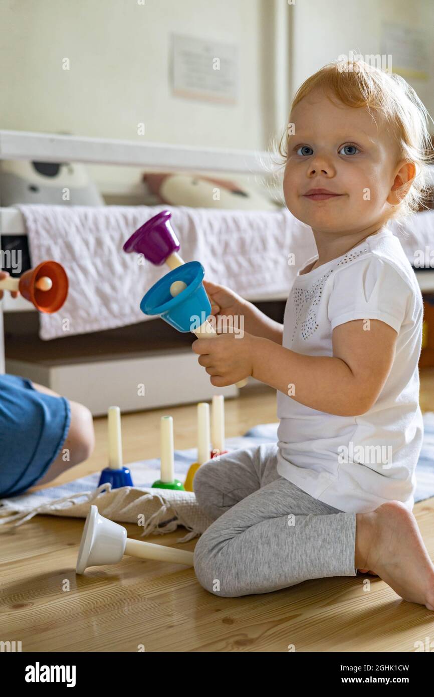 Lächelndes Baby, das farbige kindliche Handglocken spielt und die Melodie des Musikinstruments studiert Stockfoto