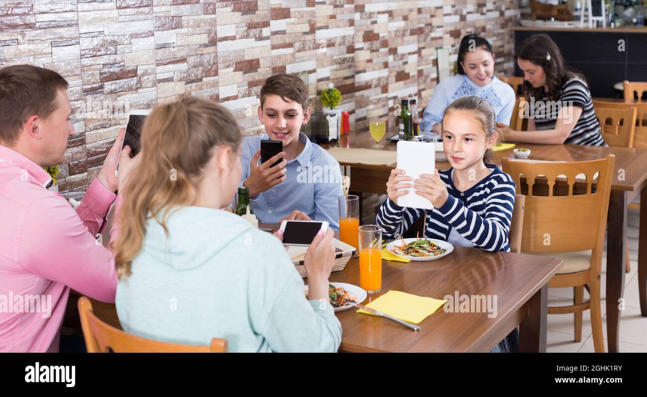 Familie beschäftigt sich mit Telefon während des Mittagessens im Familiencafe Stockfoto