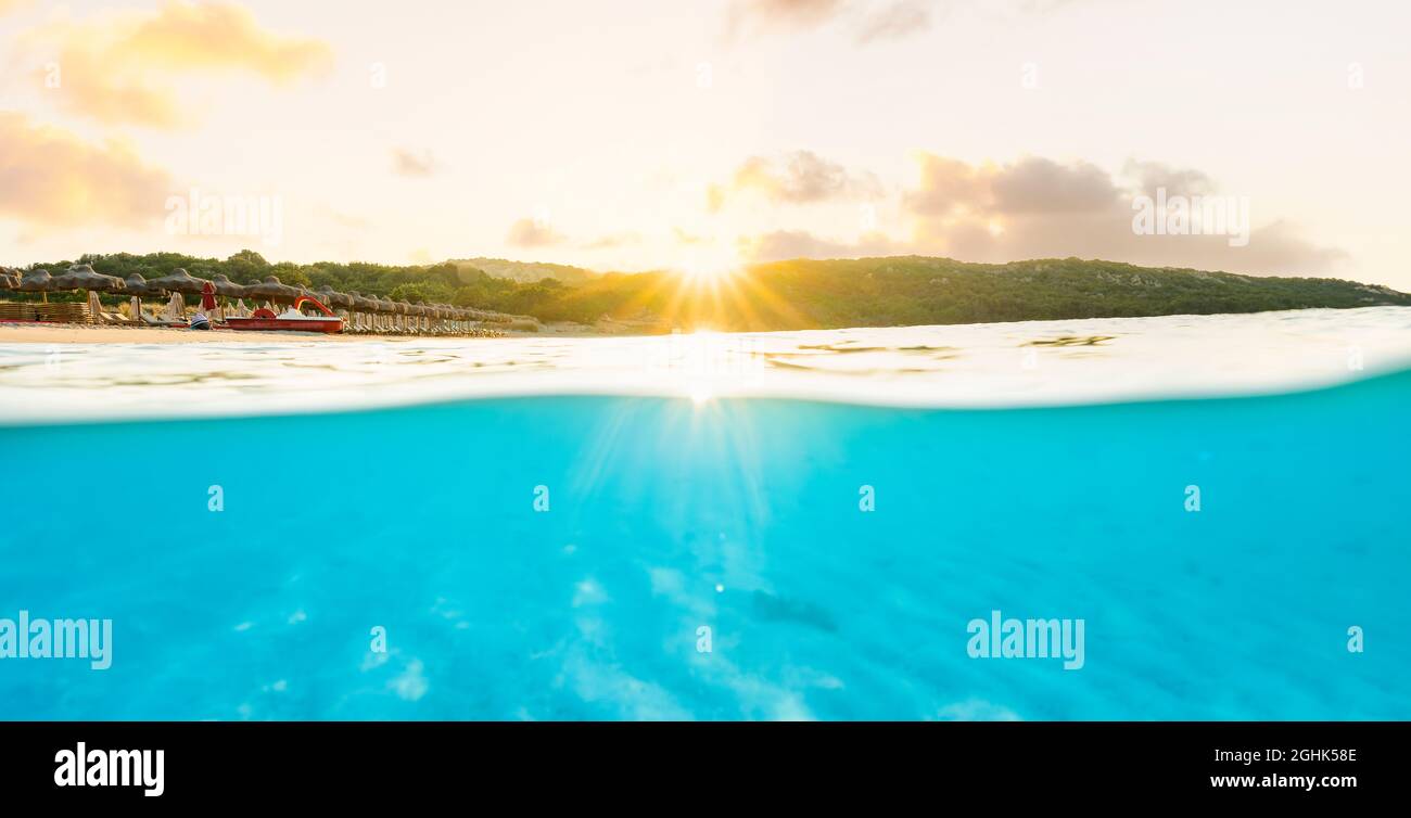 (Selektiver Fokus) Split Shot, über dem Bild. Kristallklares, türkisfarbenes Wasser und einige Sonnenschirme, die während eines atemberaubenden Sonnenaufgangs beleuchtet werden. Stockfoto