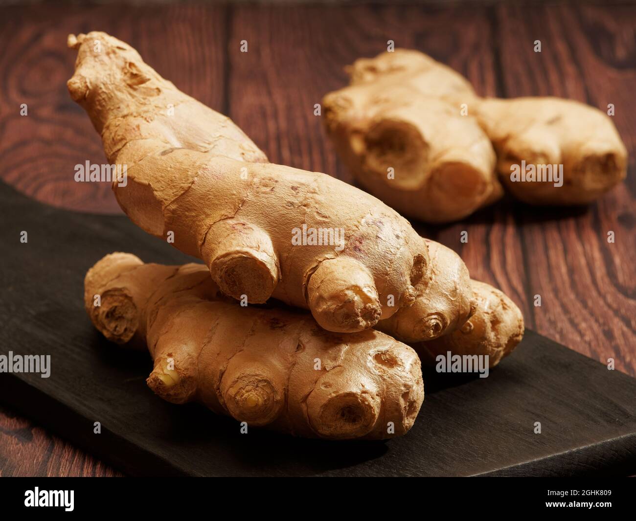 Ingwerwurzel auf einem verbrannten Holzschneidebrett auf braunem Holzhintergrund Stockfoto