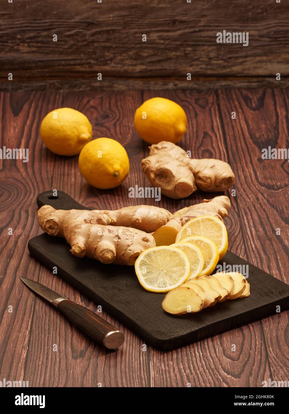 Ingwerwurzel, Scheiben Ingwerwurzel und Scheiben Zitrone auf einem verbrannten Holzschneidebrett auf braunem Holzhintergrund Stockfoto