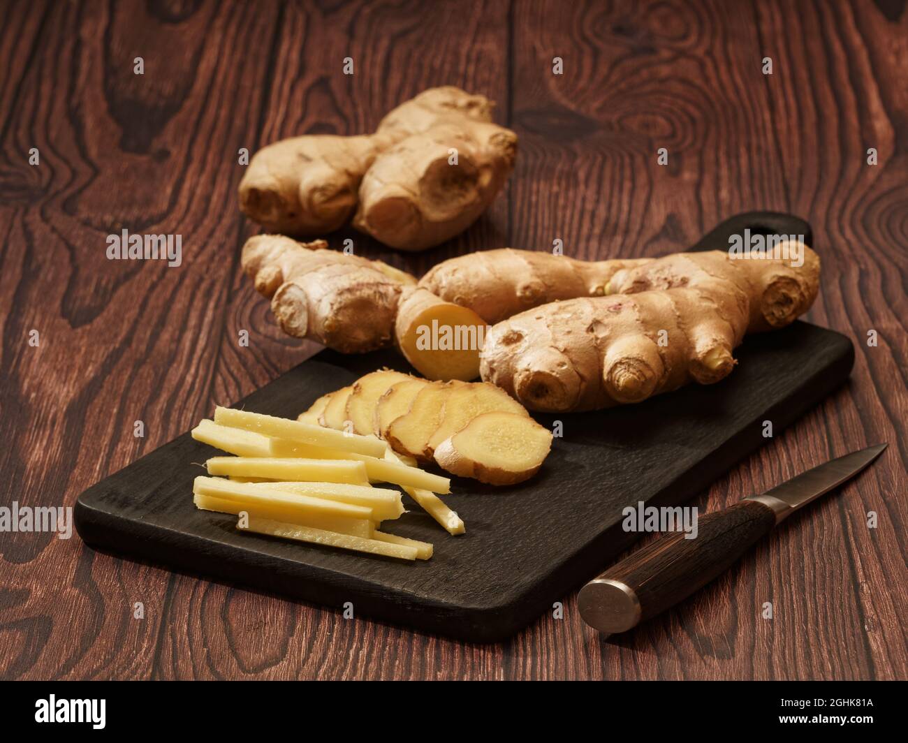 Ingwerwurzel in Streifen und Scheiben auf einem verbrannten Holzschneidebrett auf braunem Holzhintergrund geschnitten, flacher Fokus Stockfoto