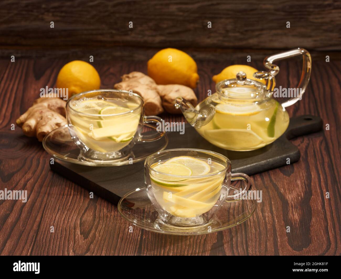 Ingwer- und Zitronentee in Glasbechern und Teekannen auf einem verbrannten Holzschneidebrett Stockfoto