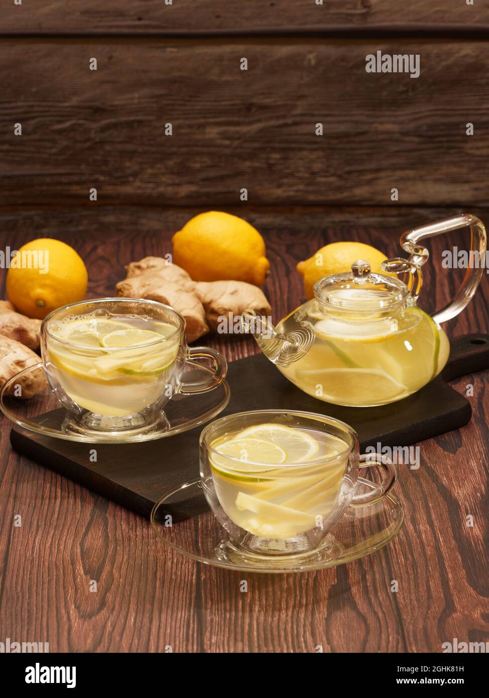 Ingwer- und Zitronentee in Glasbechern und Teekannen auf einem verbrannten Holzschneidebrett Stockfoto
