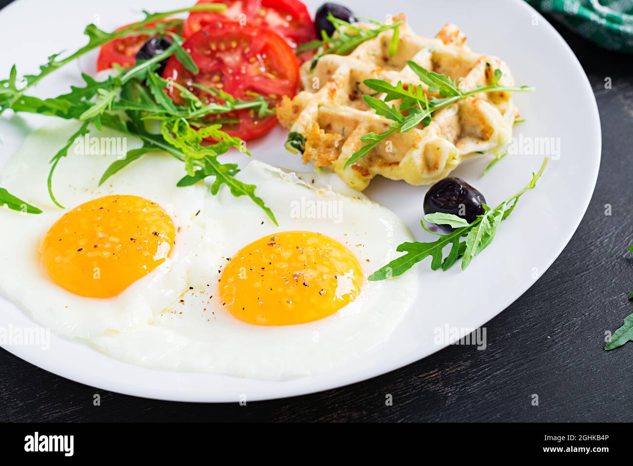 Frühstück mit Zucchini-Waffeln, Spiegeleiern, Tomaten, schwarzen Oliven und Rucola auf weißem Hintergrund. Vorspeisen, Snacks, Brunch. Gesundes vegetarisches Essen. Stockfoto