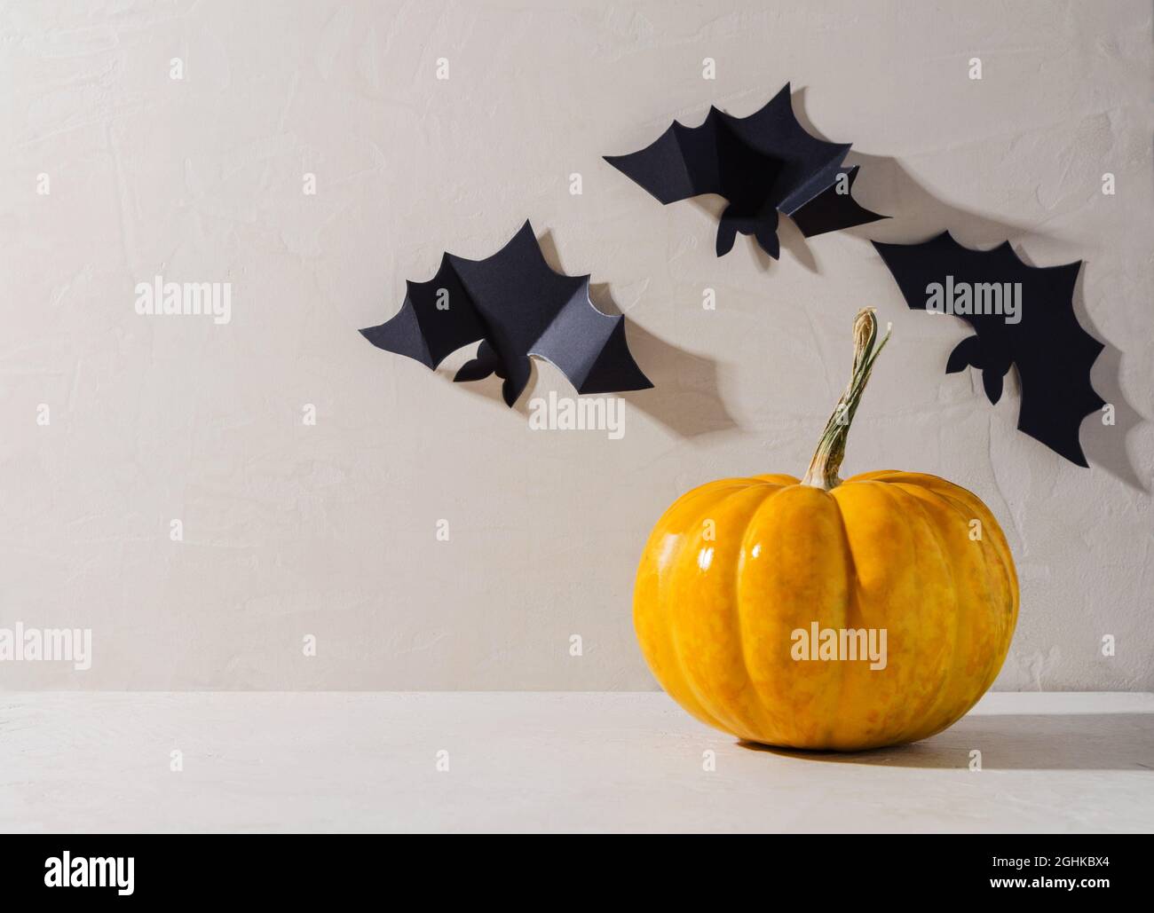 Minimalistischer Hintergrund von Halloween. Orangefarbener Kürbis und dekorative schwarze Fledermäuse auf beigem Hintergrund, Text kopieren Stockfoto