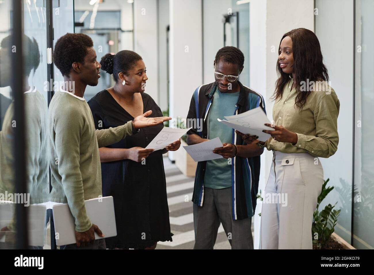 Gruppe von jungen schwarzen Geschäftsleuten, die im Korridor des modernen Büros stehen und Charts und Verkaufsberichte diskutieren Stockfoto