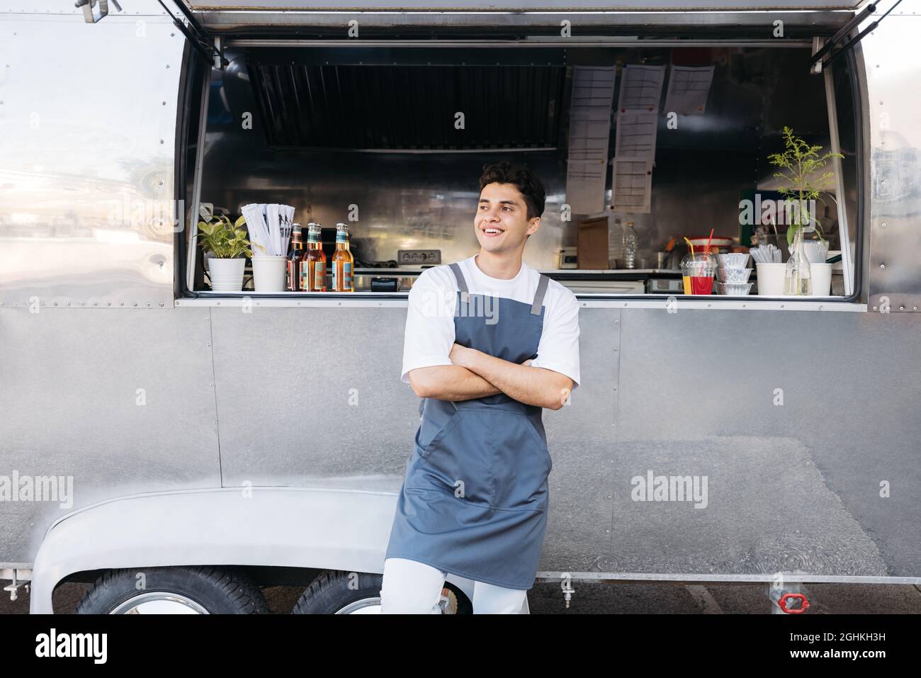 Selbstbewusster Inhaber von Kleinunternehmen im Vorfeld, der mit gekreuzten Armen steht. Verkäufer steht im Freien vor einem Food Truck. Stockfoto