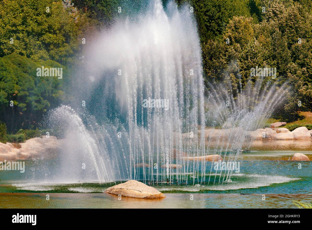 Im Dikmen Valley Park in Ankara spritzt ein großer Wasserbrunnen Wasser in die Luft. Bäume mit verschiedenen Grüntönen auf dem Hintergrund. Stockfoto