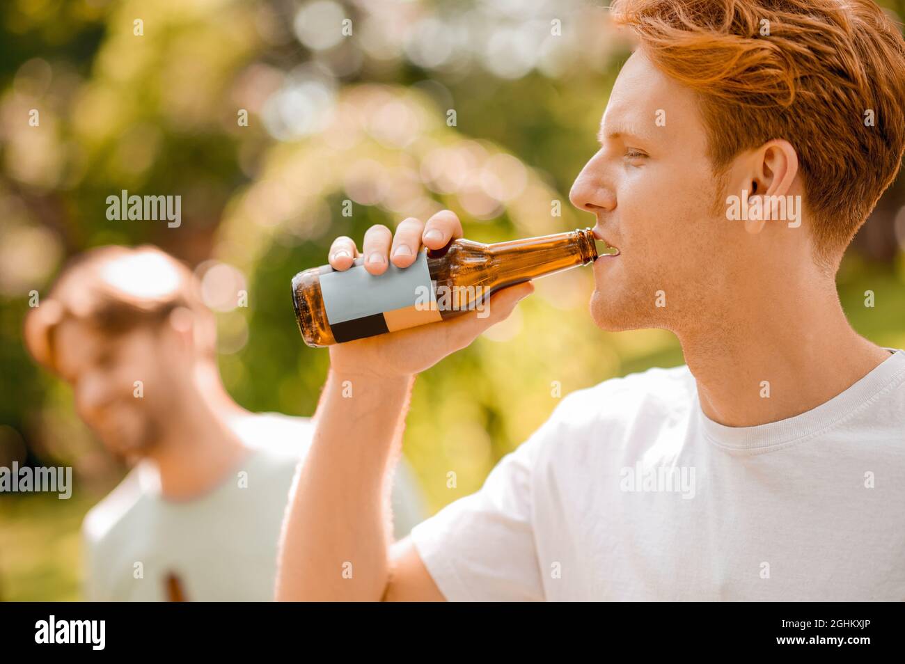 Profil des rothaarigen Mannes, der aus der Flasche trinkt Stockfoto