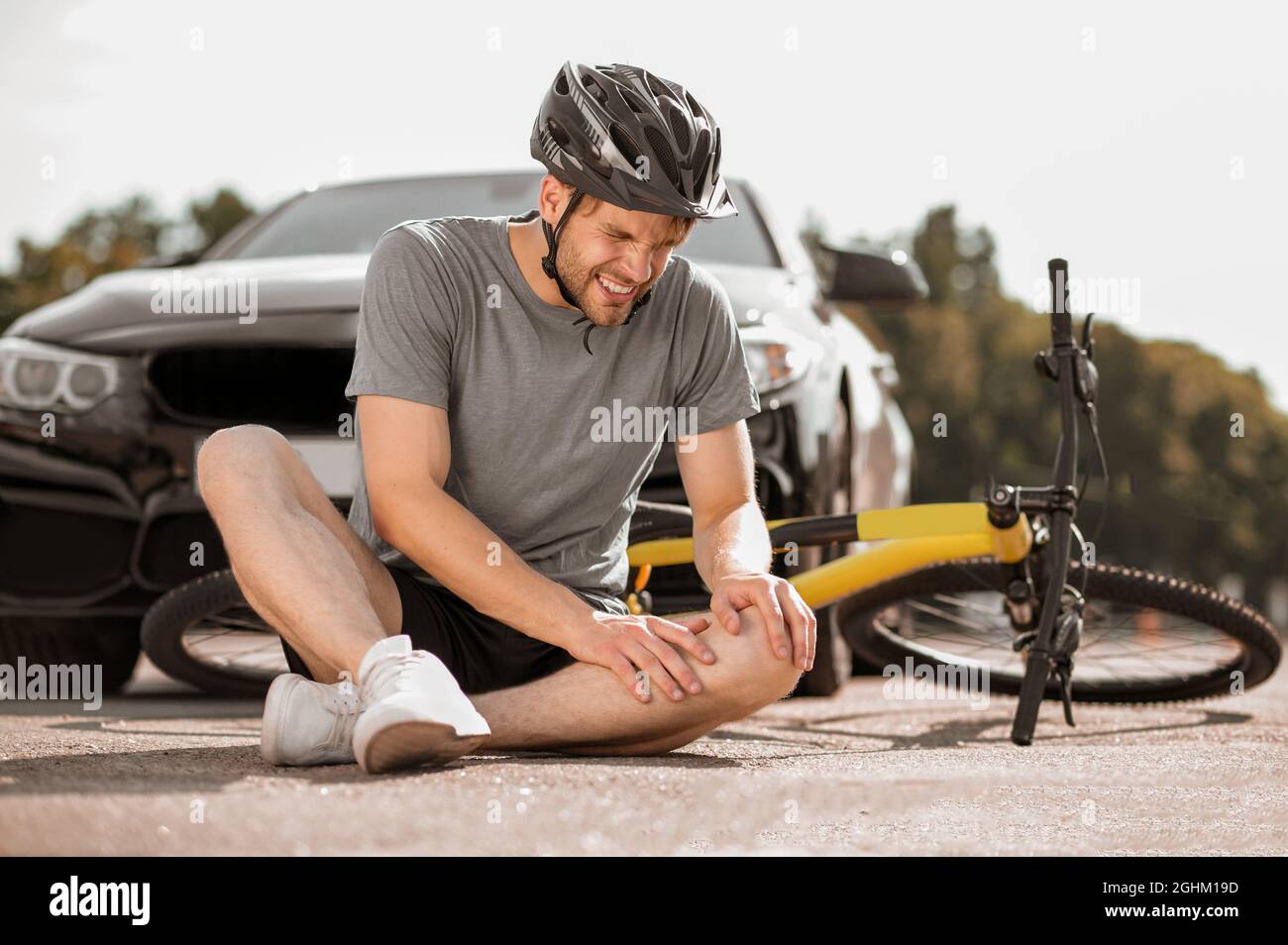 Verletzter Radfahrer, der auf der Straße in der Nähe des Autos sitzt Stockfoto