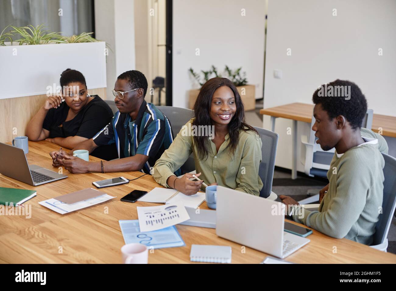 Positive junge afroamerikanische Geschäftsleute sprechen an einem großen Tisch Stockfoto