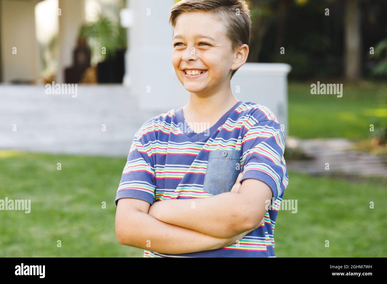Lächelnder kaukasischer Junge vor dem Haus, der im Garten von der Kamera wegschaute Stockfoto