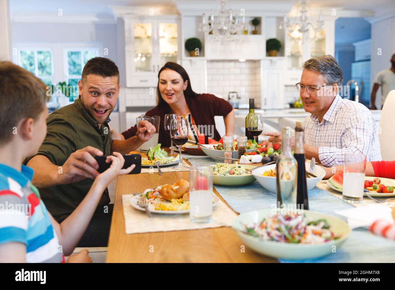 Kaukasischer Großvater und Eltern mit Tochter und Sohn, die beim Abendessen telefonieren Stockfoto