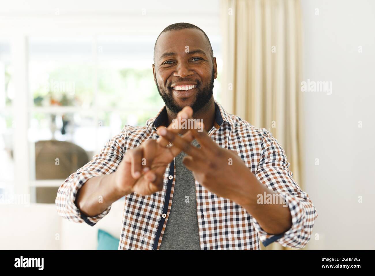 Porträt eines afroamerikanischen Mannes, der lächelt und die Kamera im Wohnzimmer anschaut und die Gebärdensprache spricht Stockfoto