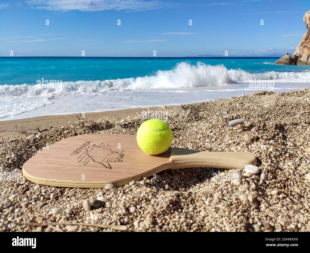 Matkot griechisches Paddle Beach Tennis Spiel mit Ball und Holzschläger mit Karte der Insel Lefkada, Griechenland. Sportausrüstung am Sandstrand mit türkisfarbenem Wasser Stockfoto