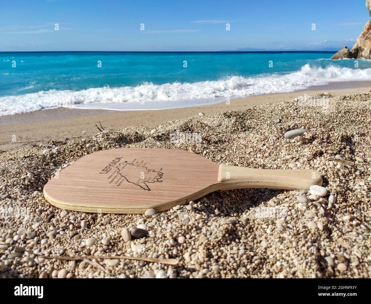 Matkot griechischer Paddle Beach Tennis Spiel Holzschläger mit Karte der Insel Lefkada, Mylos Strand mit türkisfarbenem Wasser und weißen Wellen. Sportausrüstung an Stockfoto