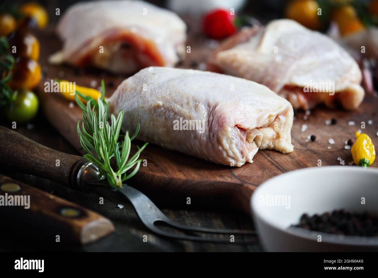 Rohes, ungekochenes Hühnchen-Oberschenkelfleisch über einem Holzschneidebrett mit frischen Zutaten. Extrem selektiver Fokus mit verschwommenem Vorder- und Hintergrund. Stockfoto