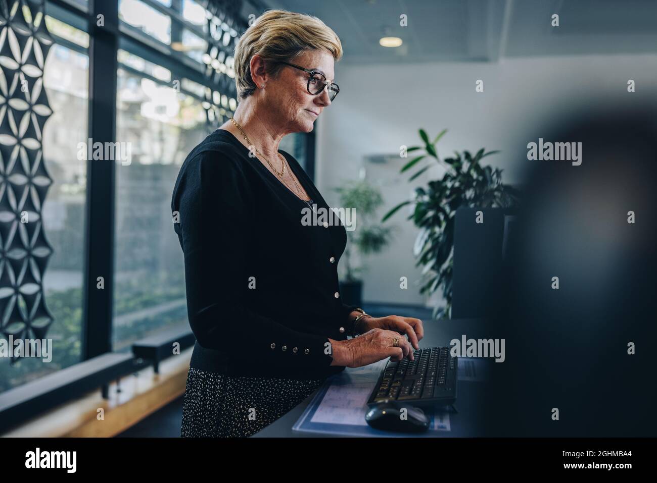 Leitende Geschäftsfrau, die im Büro arbeitet. Reife weibliche professionelle Arbeit am Stehtisch im modernen Büro. Stockfoto