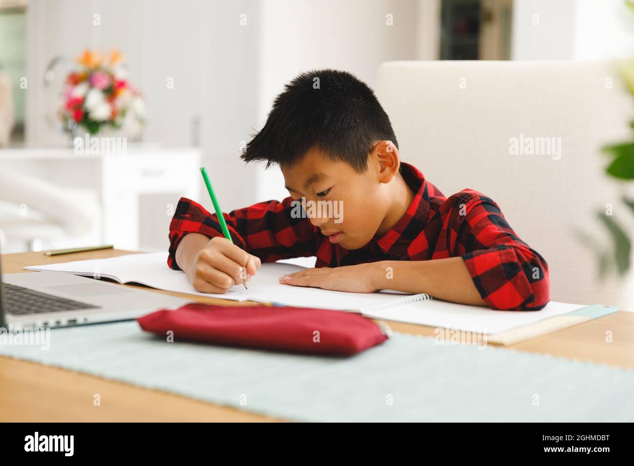 Asiatischer Junge sitzt am Tisch und mit Laptop während des Online-Unterrichts Stockfoto