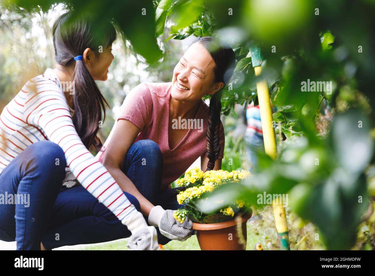 Glückliche asiatische Mutter und Tochter lächeln, tragen Handschuhe und arbeiten im Garten Stockfoto