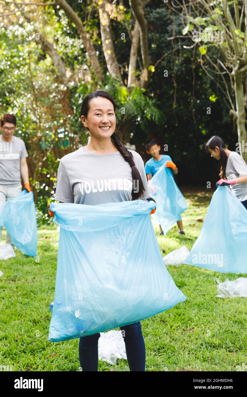 Porträt einer lächelnden asiatischen Mutter, die mit der Familie auf dem Land Müll in Müllsäcke legt Stockfoto