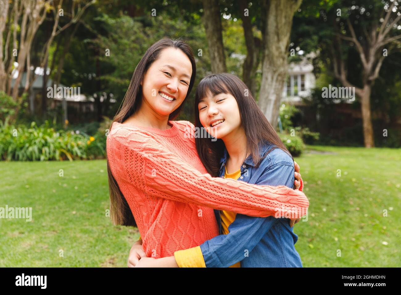Porträt einer glücklichen asiatischen Mutter, die ihre Tochter umarmt und im Garten lächelt Stockfoto