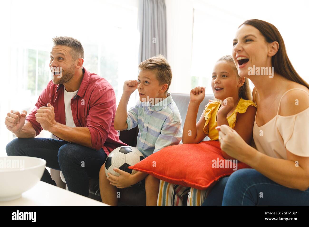 Aufgeregte kaukasische Eltern auf der Couch mit Tochter und Sohn, die sich ein Fußballspiel im fernsehen ansahen und jubelten Stockfoto