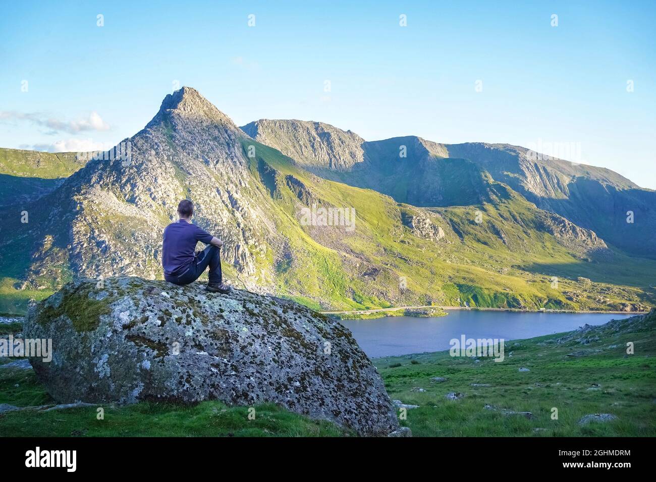 Rückansicht eines isolierten Wanderers auf Felsen mit Blick über den Lake Ogwen zum Mount Tryfan am sonnigen Sommertag, Snowdonia National Park, N. Wales, Großbritannien. Stockfoto