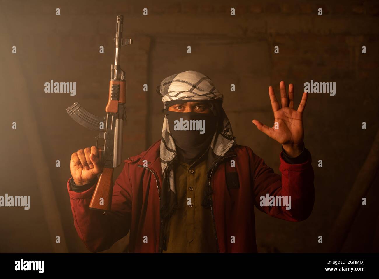 Militant oder Gangster mit Gesichtsschutz und Waffe in der Hand, die sich durch das Auflegen der Hände ergeben. Stockfoto