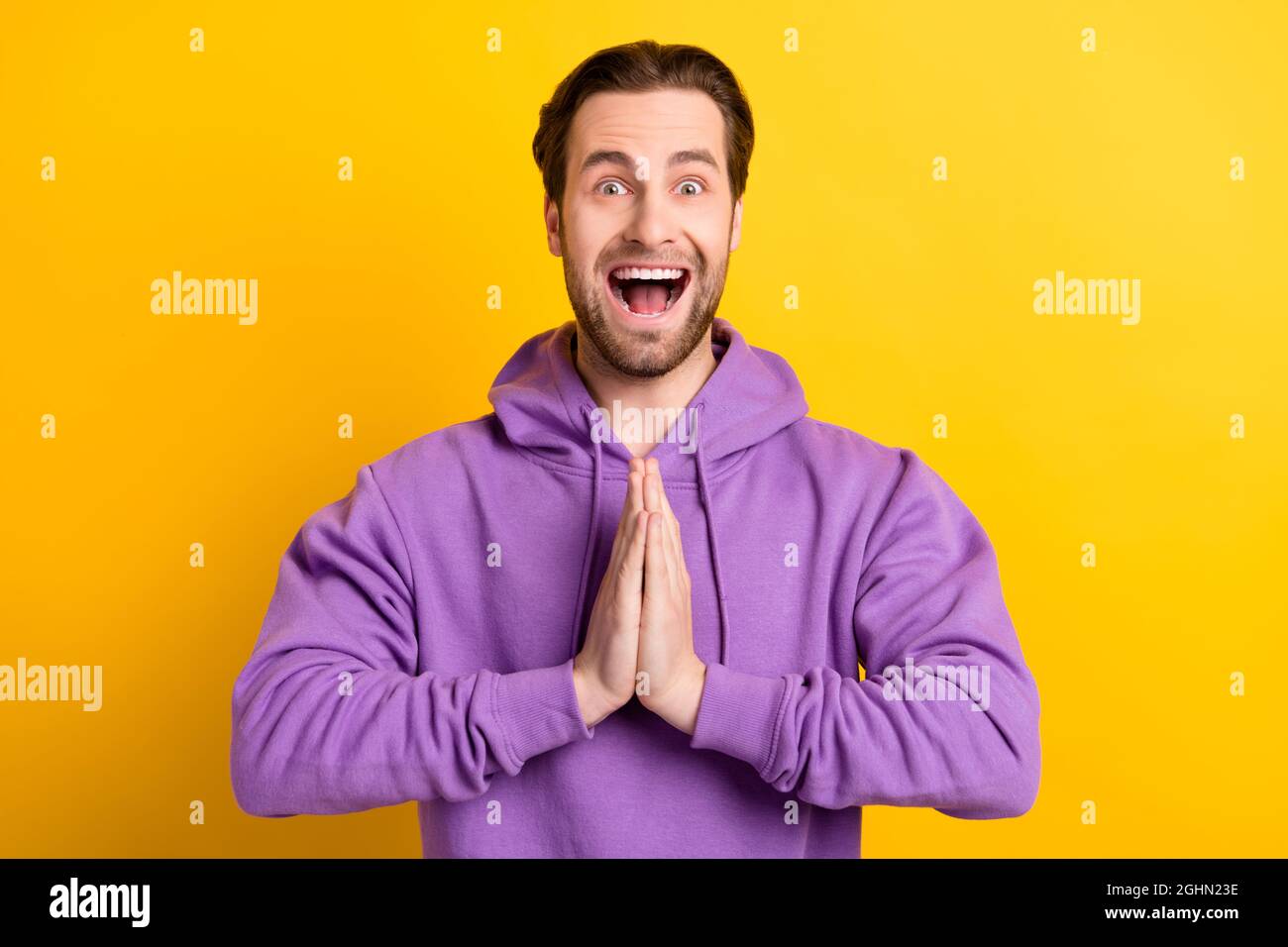 Foto von glücklichen verrückten Kerl halten Hände Plead Anfrage offenen Mund tragen violette Sweatshirt isoliert gelbe Farbe Hintergrund Stockfoto