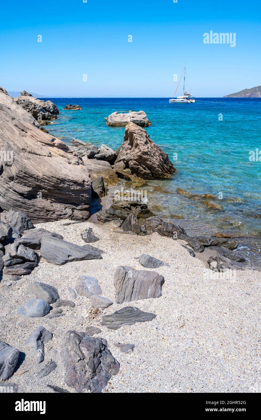 Strand mit vulkanischen Felsen, türkisfarbenem Meer, Segel-Katamaran dahinter, Gyali, Dodekanes, Griechenland Stockfoto