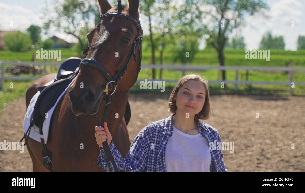 Ein junges Mädchen in einem nicht geknöpften Hemd und einem weißen T-Shirt hält ein Pferd an den Zügeln. Hochwertige Fotos Stockfoto