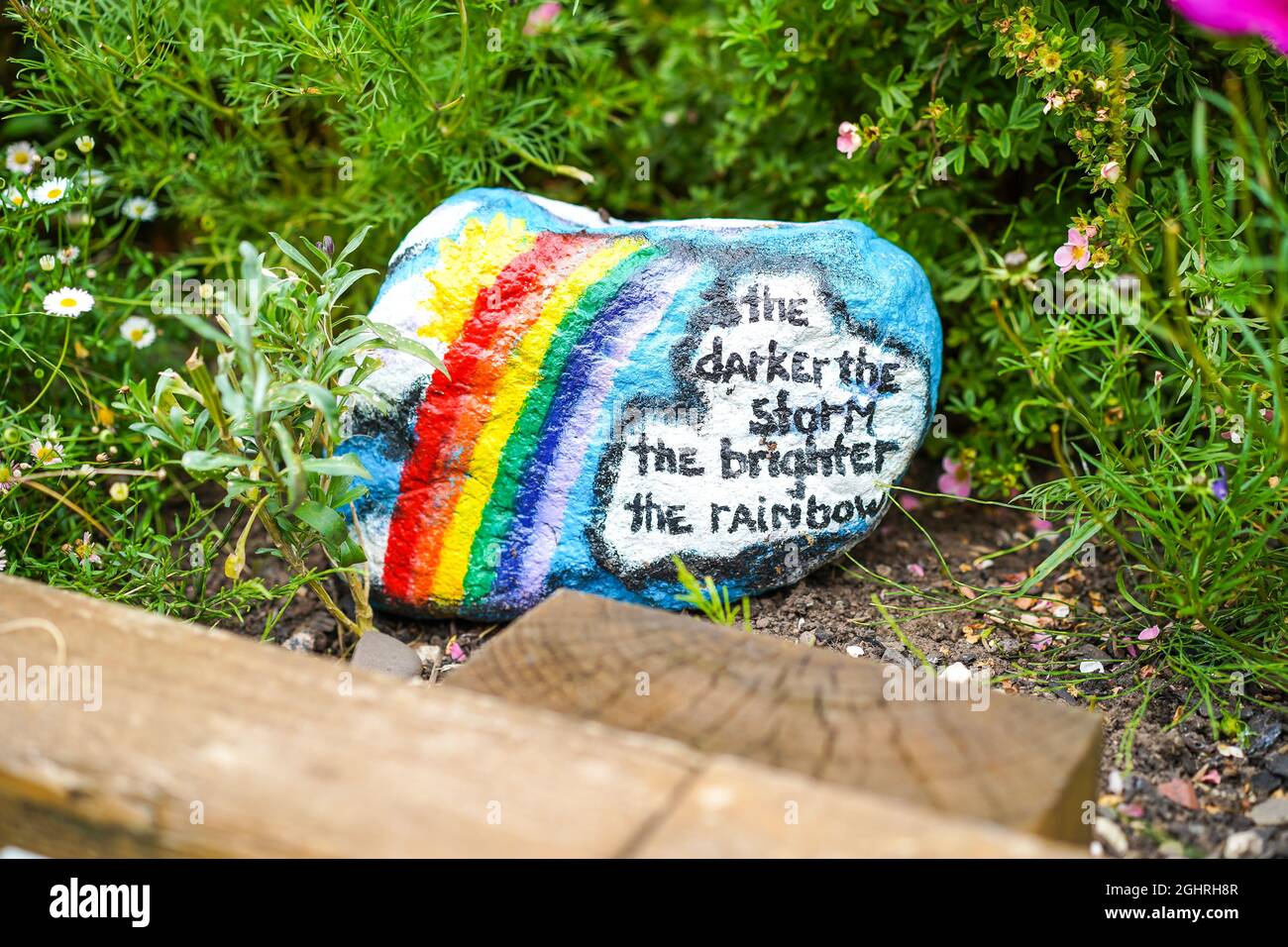 „je dunkler der Sturm, desto größer der Regenbogen“ – Schild auf einem Gartenstein, auf dem Passanten lesen und sich positiv denken, denken und verhalten können. Stockfoto