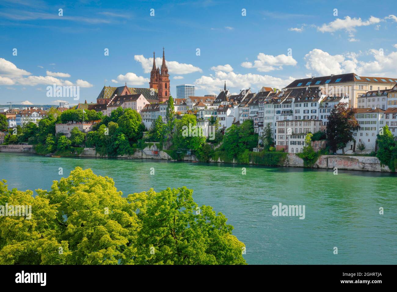 Blick auf den Basler Dom mitten in der Altstadt von Basel mit dem türkisfarbenen Rhein im Vordergrund Stockfoto