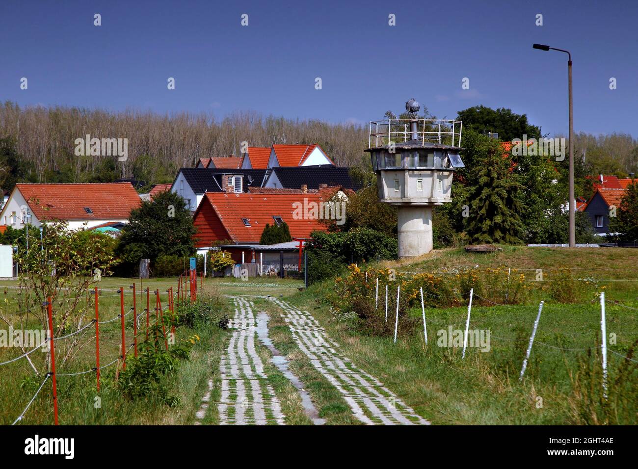 Grenzbefestigung mit Säulengang, Lochplattenweg, Beobachtungsturm der DDR-Grenztruppen, Grenzwächter und Häuser von Stockfoto