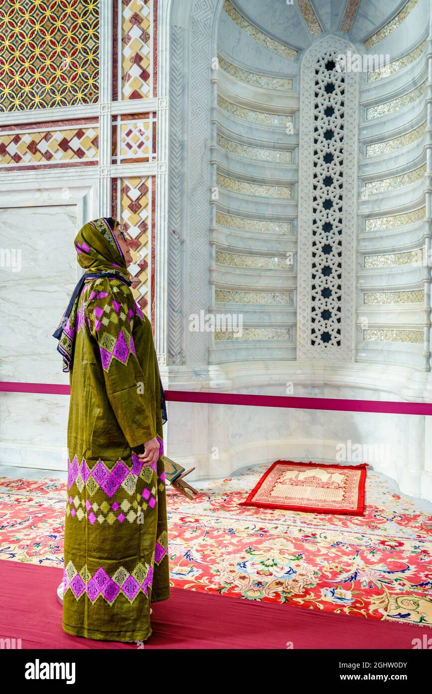 Eine Frau, die in einem traditionellen omanischen Abaya gekleidet ist und eine verzierte Nische an der Muhammad al-Amin Moschee in Maskat, Oman, anschaut Stockfoto