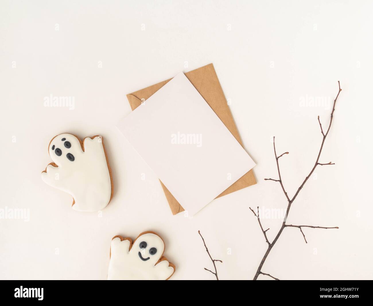 Leere weiße Postkarte und Bastelumschlag und Halloween Lebkuchen-Kekse Geister auf weißem Hintergrund. Halloween-Konzept. Draufsicht. Speicherplatz kopieren Stockfoto
