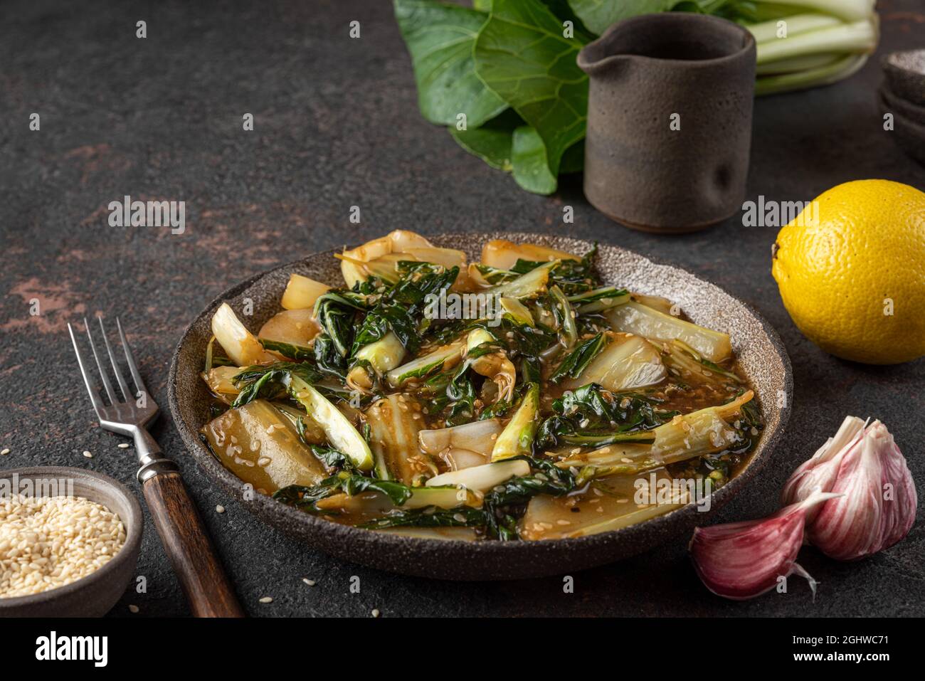 Bok Choy Gemüse unter Rühren braten mit Sojasauce und Sesam auf dunklem Hintergrund. Chinesische Küche. Gesundes veganes Essen. Nahaufnahme Stockfoto