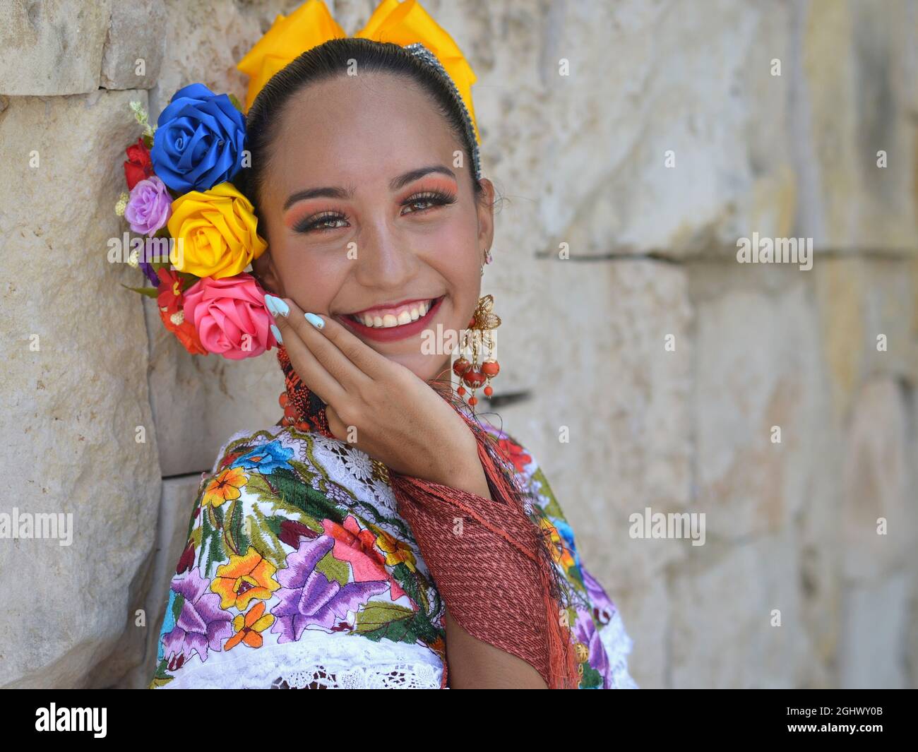 Junge schöne mexikanische Frau mit Make-up trägt traditionelles Maya Yucatecan folklorisches Kleid mit Blumen im Haar und lächelt für die Kamera. Stockfoto