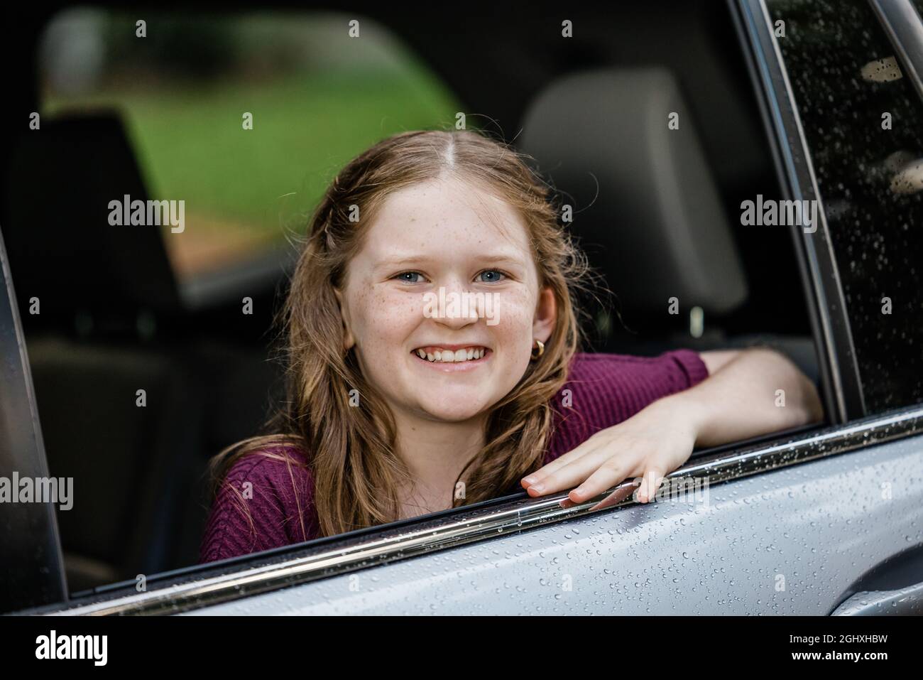 Kleines kaukasisches Mädchen mit Sommersprossen und einem lila Hemd, das aus einem Autofenster schaut Stockfoto