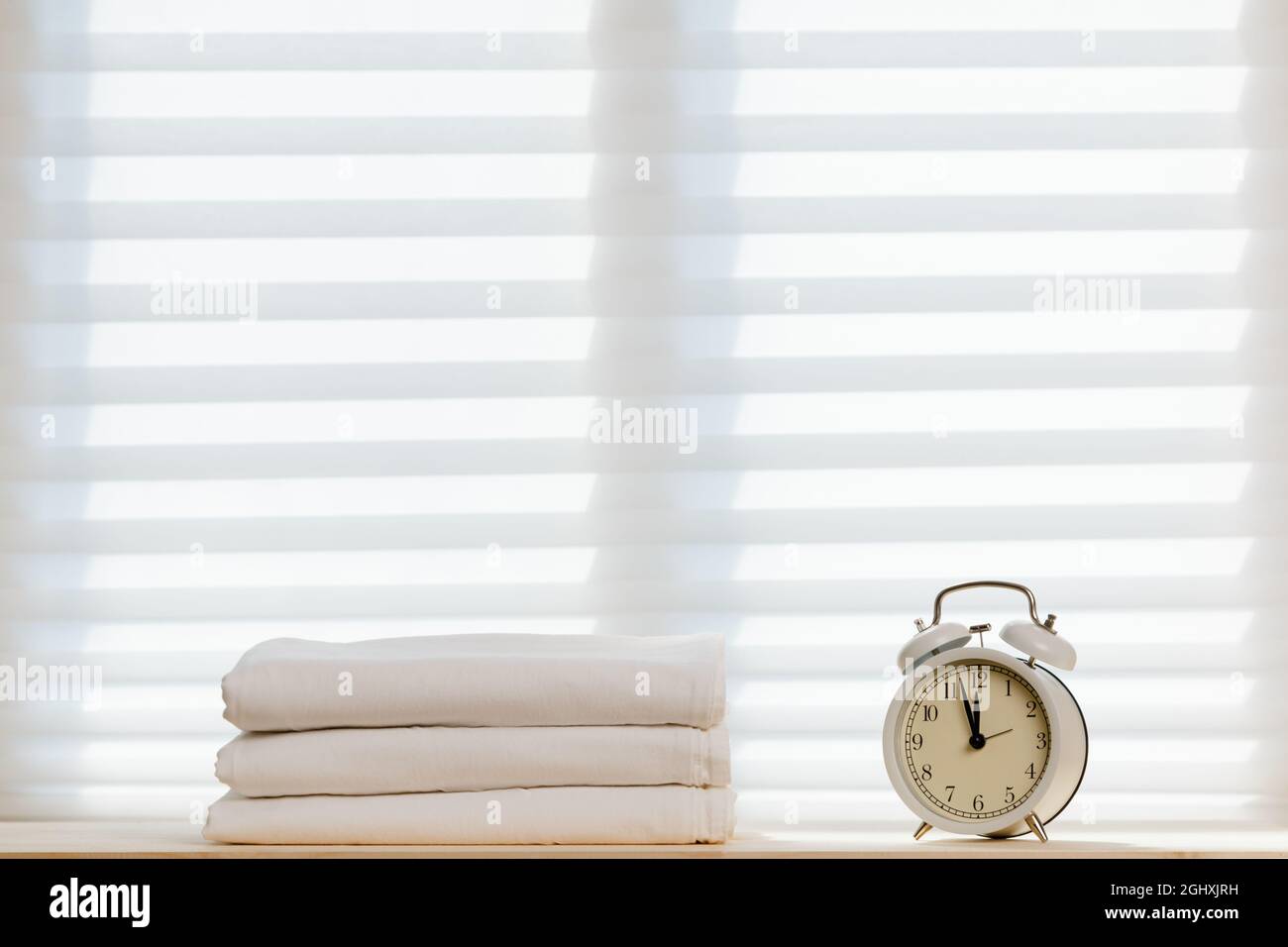 Weiße Bettwäsche, Bettwäsche und ein Wecker auf dem Hintergrund des Fensters. Stockfoto